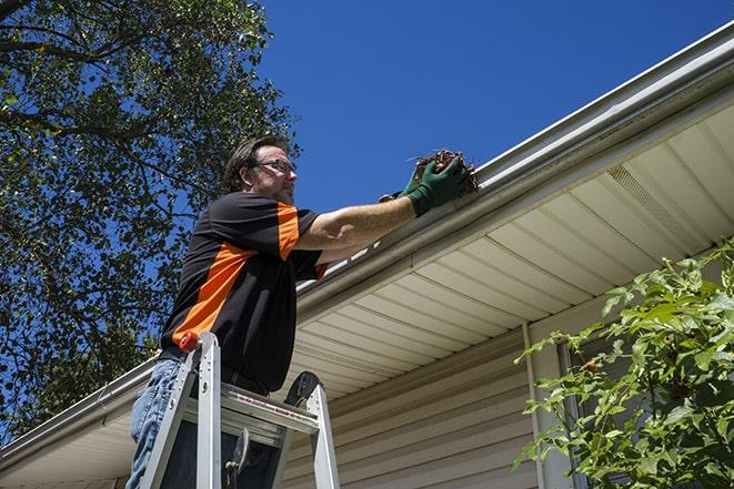 workman on a ladder repairing a broken gutter in Belchertown, MA